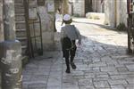 ילד חסידי עם פאות וכיפה לבנה רץ ברחוב מאה שערים בירושלים